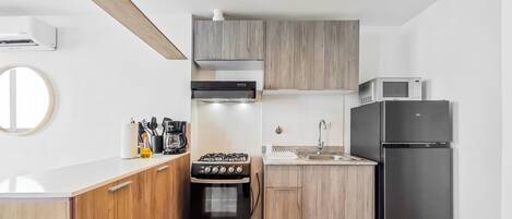 A compact kitchen with a gas stove, oven, microwave, and refrigerator.