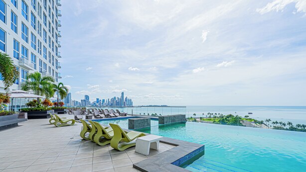 A rooftop pool area with lounge chairs, a small table, and a view of the city skyline and ocean. - The Sands by Wynwood House (Panama City)