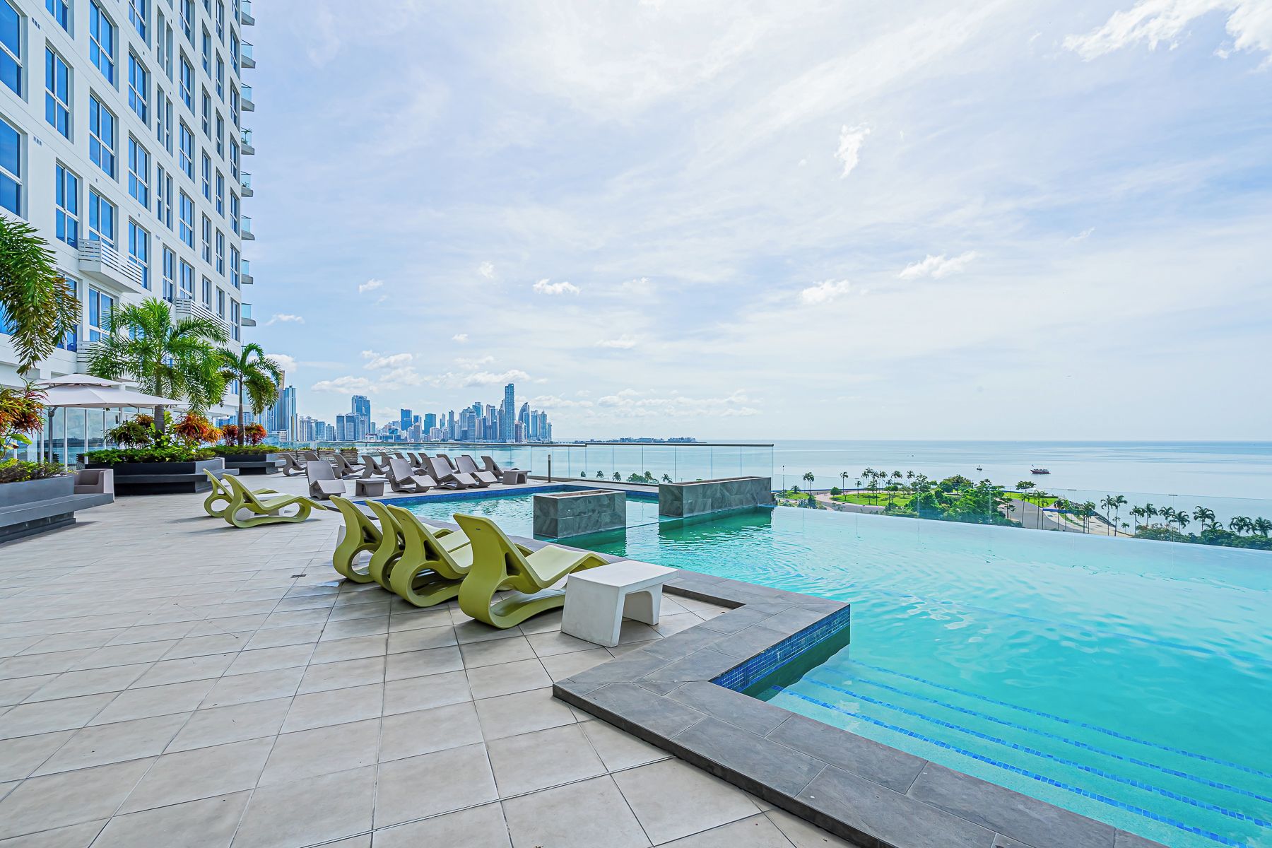 Una piscina en la azotea con sillones y vistas a un horizonte urbano.