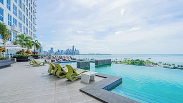 Una piscina en la azotea con sillones y vistas a un horizonte urbano.