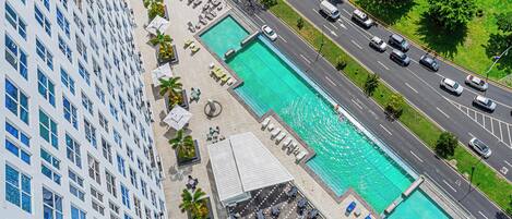 Un hôtel de grande hauteur doté d’une piscine sur le toit, de plusieurs piscines et situé près d’une route où circulent des véhicules.