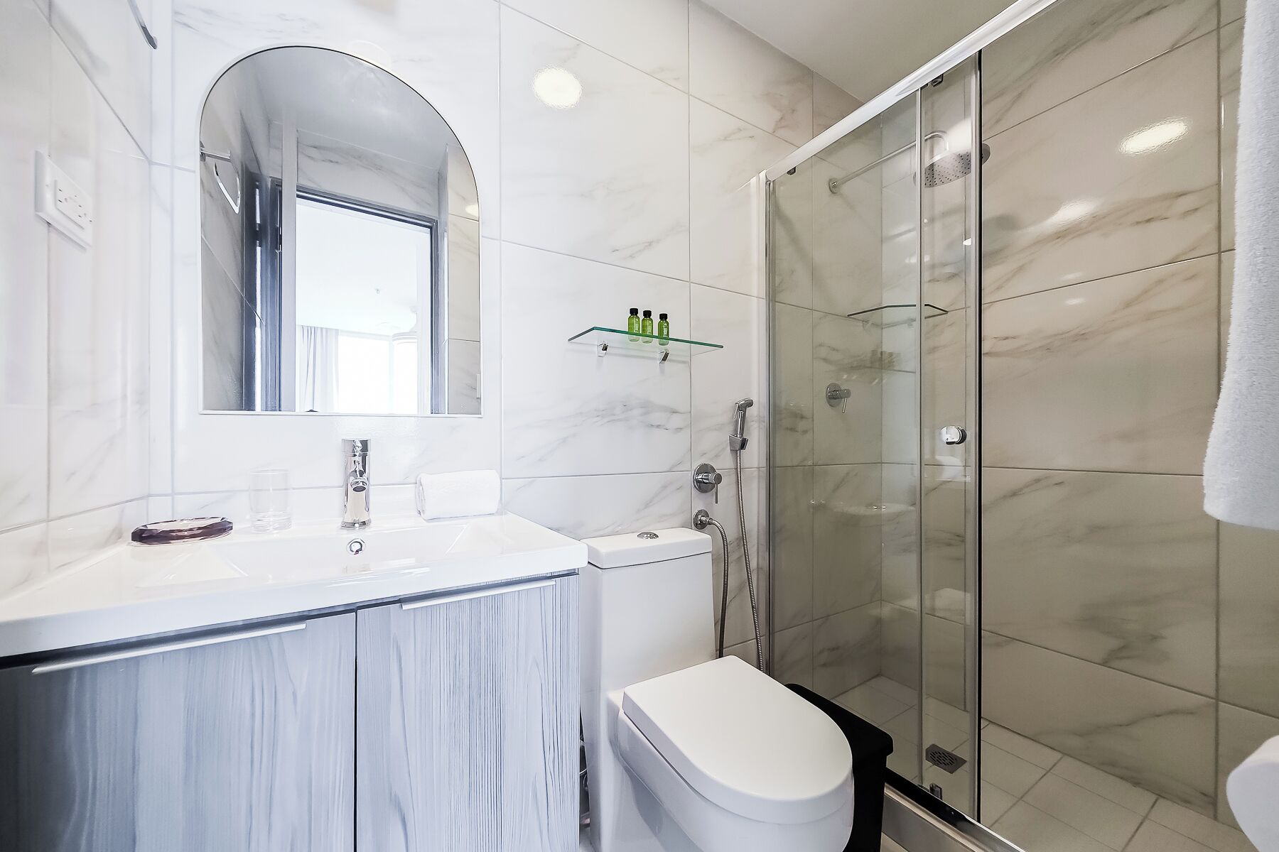 A modern bathroom with a glass shower enclosure, a marble vanity, and a toilet.