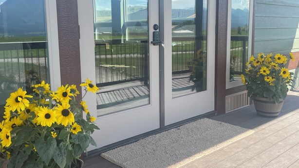A building entrance with a glass door, a wooden porch, and two potted sunflowers.