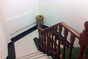 A wooden staircase with a handrail, a trash bin, and a patterned floor. - Jinqilin Hostel (Shanghai Waigaoqiao Free Trade Zone) (Shanghai)