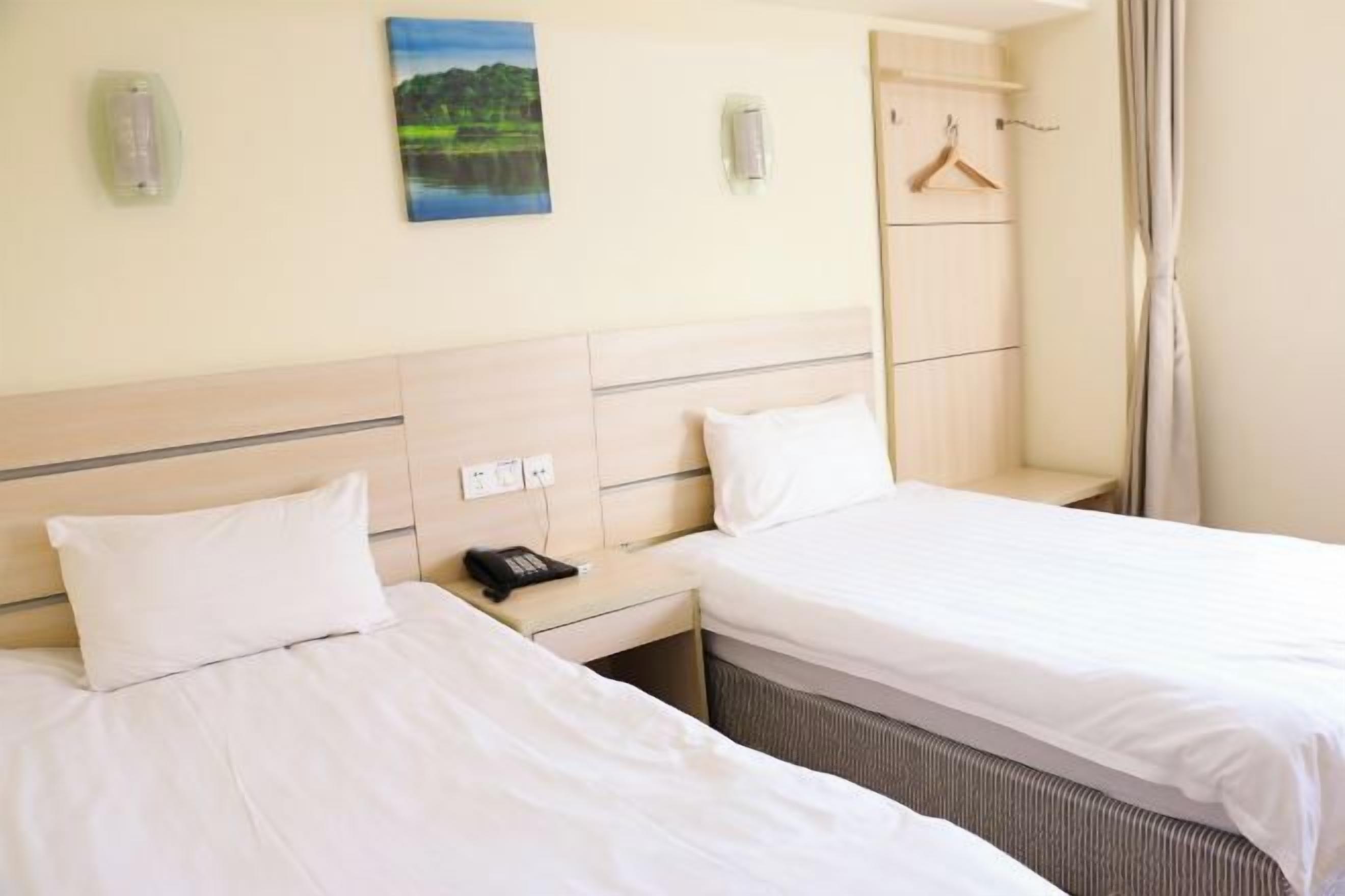 Quarto de hotel com duas camas, mesa de cabeceira com telefone, cabideiro e um quadro na parede.