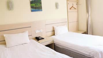 Quarto de hotel com duas camas, mesa de cabeceira com telefone, cabideiro e um quadro na parede.