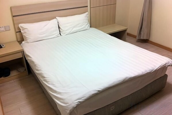 A neatly made bed with a white sheet and two pillows, a bedside table with a lamp, and a wooden floor. - Jinqilin Hostel (Shanghai Waigaoqiao Free Trade Zone) (Shanghai)