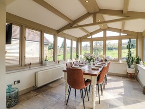A dining area with a long table set for six, large windows, and a view of the garden.