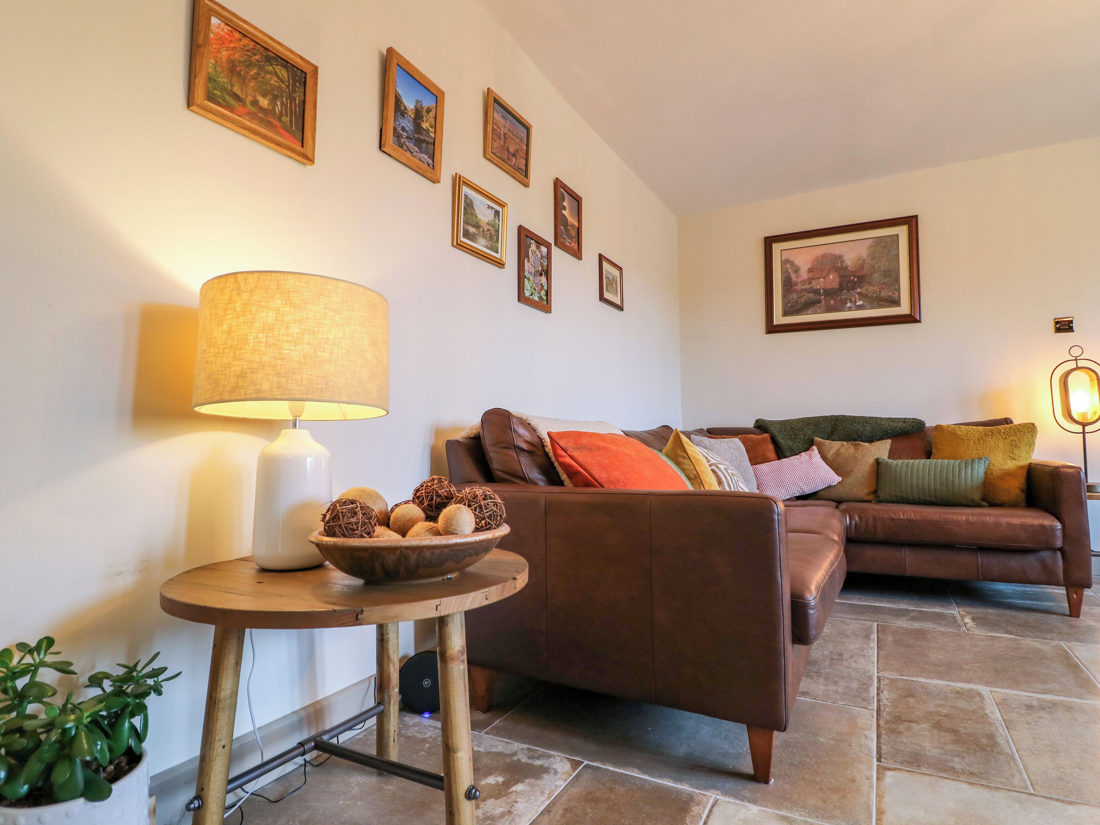 Un salón con un sofá de cuero marrón, una mesa redonda de madera con una lámpara y un cuenco con bolas decorativas.