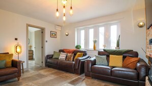 A spacious living room with leather sofas, a coffee table, and a fireplace. There are multiple windows providing natural light, and a door leading to another room. - Cherry Tree Farm (Chesterfield)