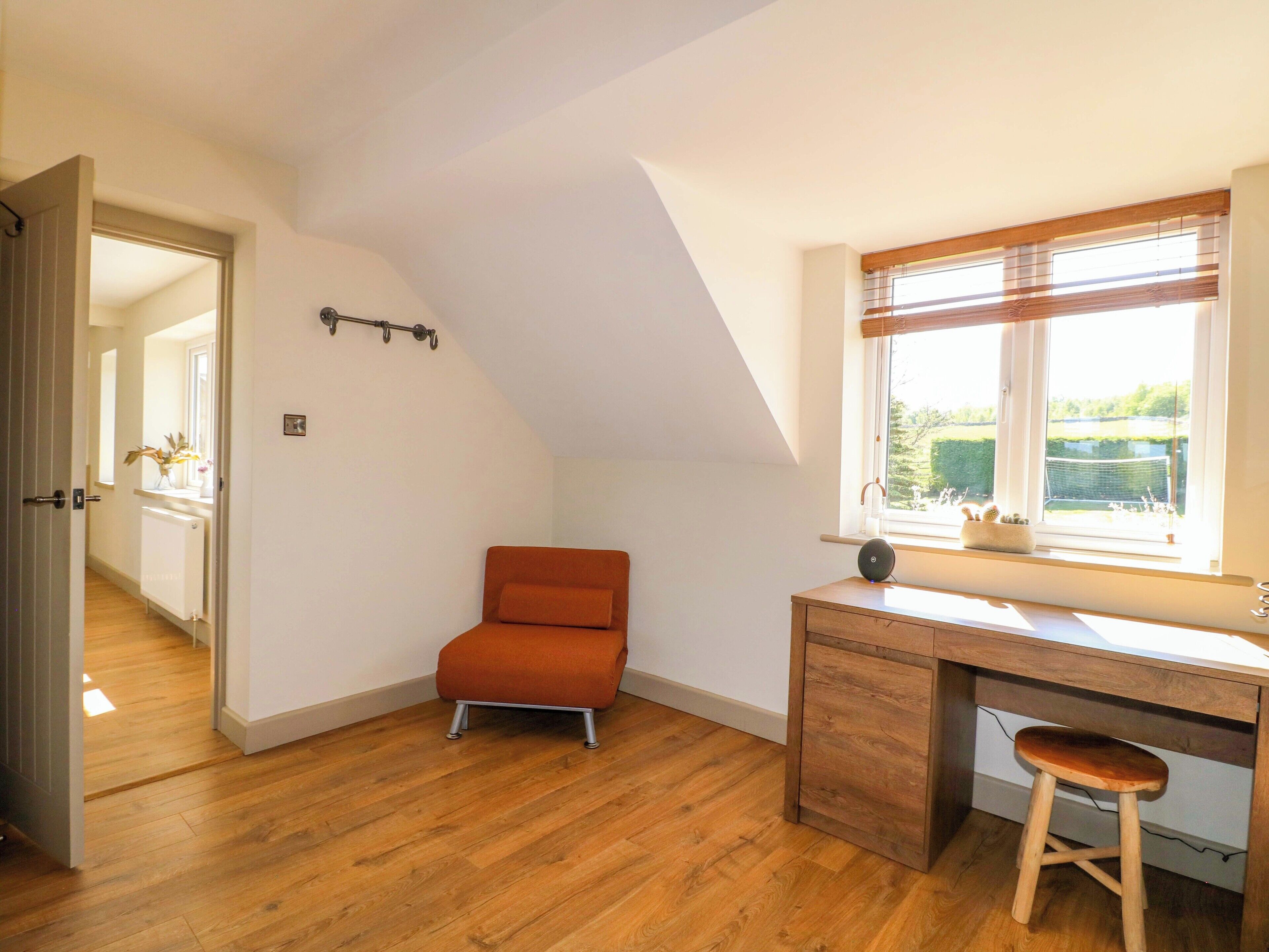 Una habitación con techo inclinado, un escritorio de madera con taburete, un radiador y una ventana con persianas.