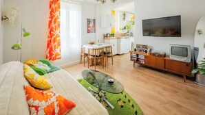 Una sala moderna con un sofá, una mesa de centro de vidrio, un comedor con sillas, una cocina y un televisor.