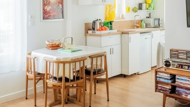 Una cocina moderna con armarios blancos, un comedor con mesa de vidrio y una lámpara de araña.