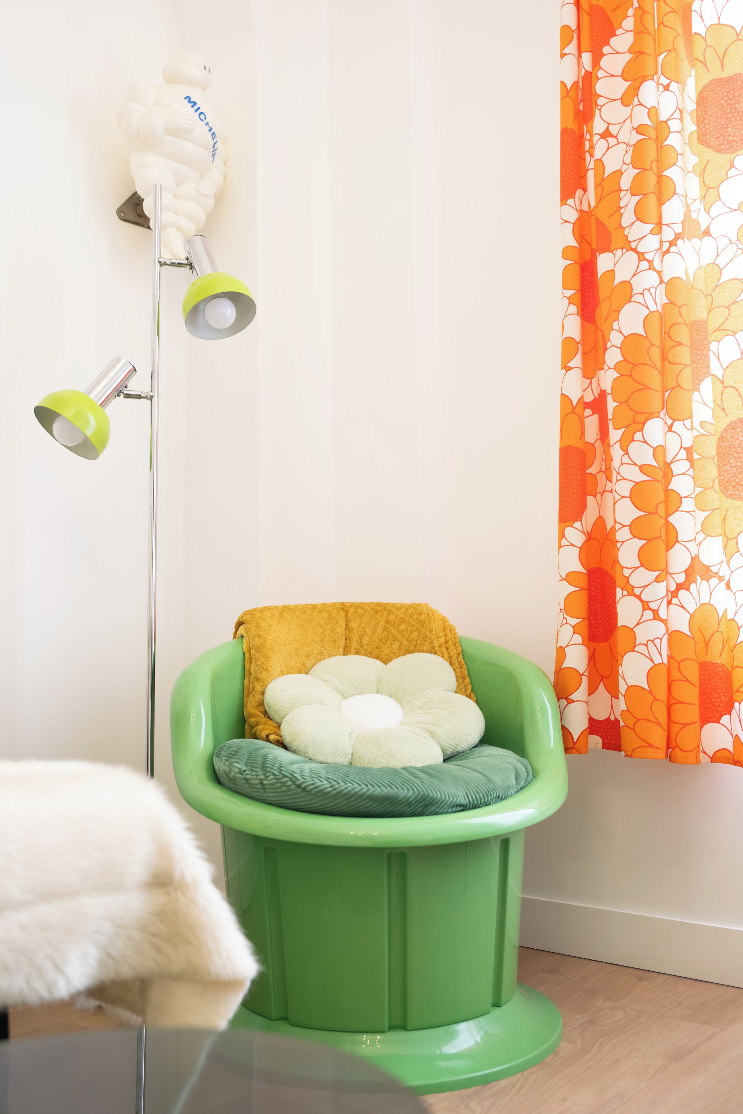 A green pet bed with a cushion, a floor lamp, and a curtain with a floral pattern.