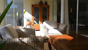 A sunlit room with wicker furniture, a wooden cabinet, and a sliding glass door leading to an outdoor area. - Jardins do Golfe at Vale do Lobo (Loulé)