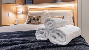Un letto rifatto con asciugamani bianchi arrotolati, una coperta blu fantasia e una testiera in legno.