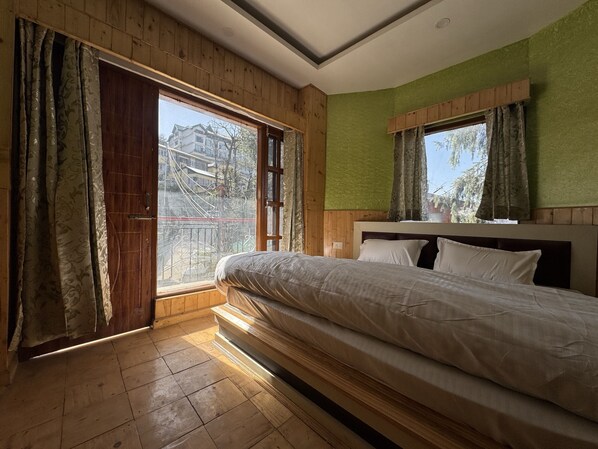 A bedroom with a large bed, wooden flooring, a green accent wall, and a window with curtains.