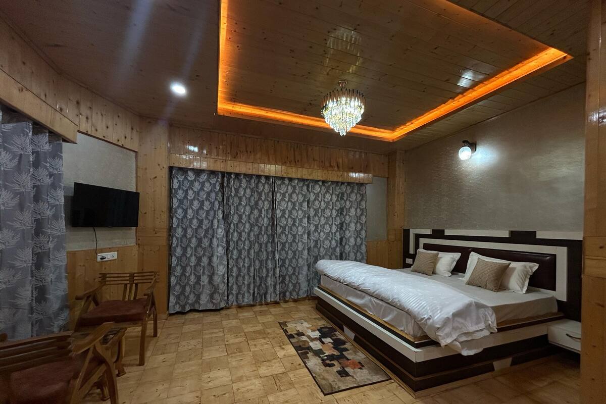 A bedroom with a bed, a TV, wooden walls, a chandelier, and a patterned curtain.