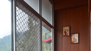 A room with a large window, a wooden chair, a small table with a laptop, and a potted plant. - Nature Heaven Homestay (Shimla)