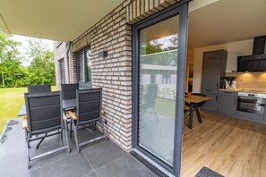 Une cuisine moderne dotée d’une grande fenêtre, un coin repas avec des chaises et une terrasse avec une table et des chaises.