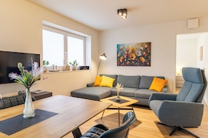 Un soggiorno moderno con un divano, un tavolo da pranzo, una TV e un quadro appeso al muro.
