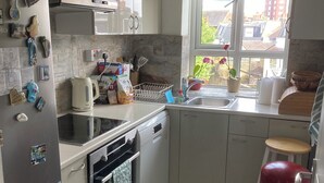 A modern kitchen with white cabinets, a stainless steel refrigerator, a dishwasher, and a red trash can.