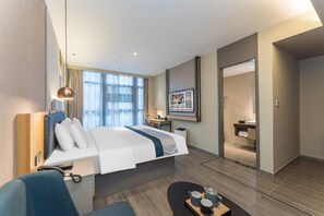A modern hotel room with a bed, bedside table, lamp, and a view of the bathroom.