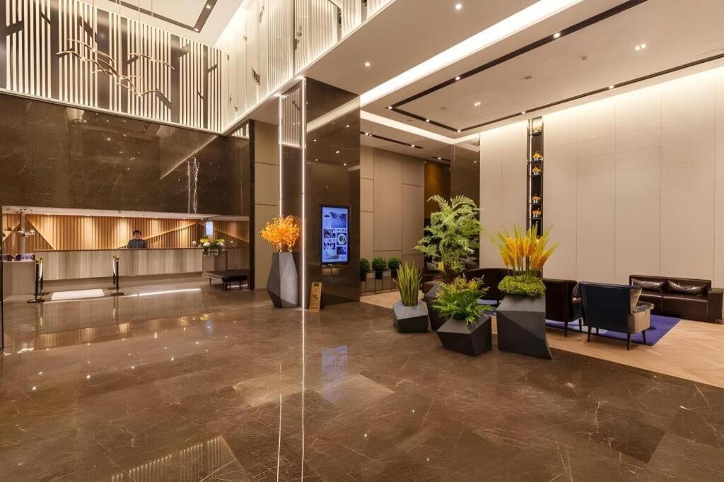 A modern hotel lobby with a reception desk, seating area, and a staircase.
