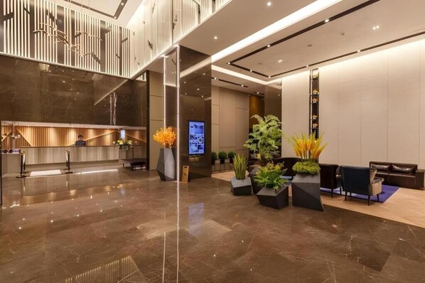 A modern hotel lobby with a reception desk, seating area, and a staircase.