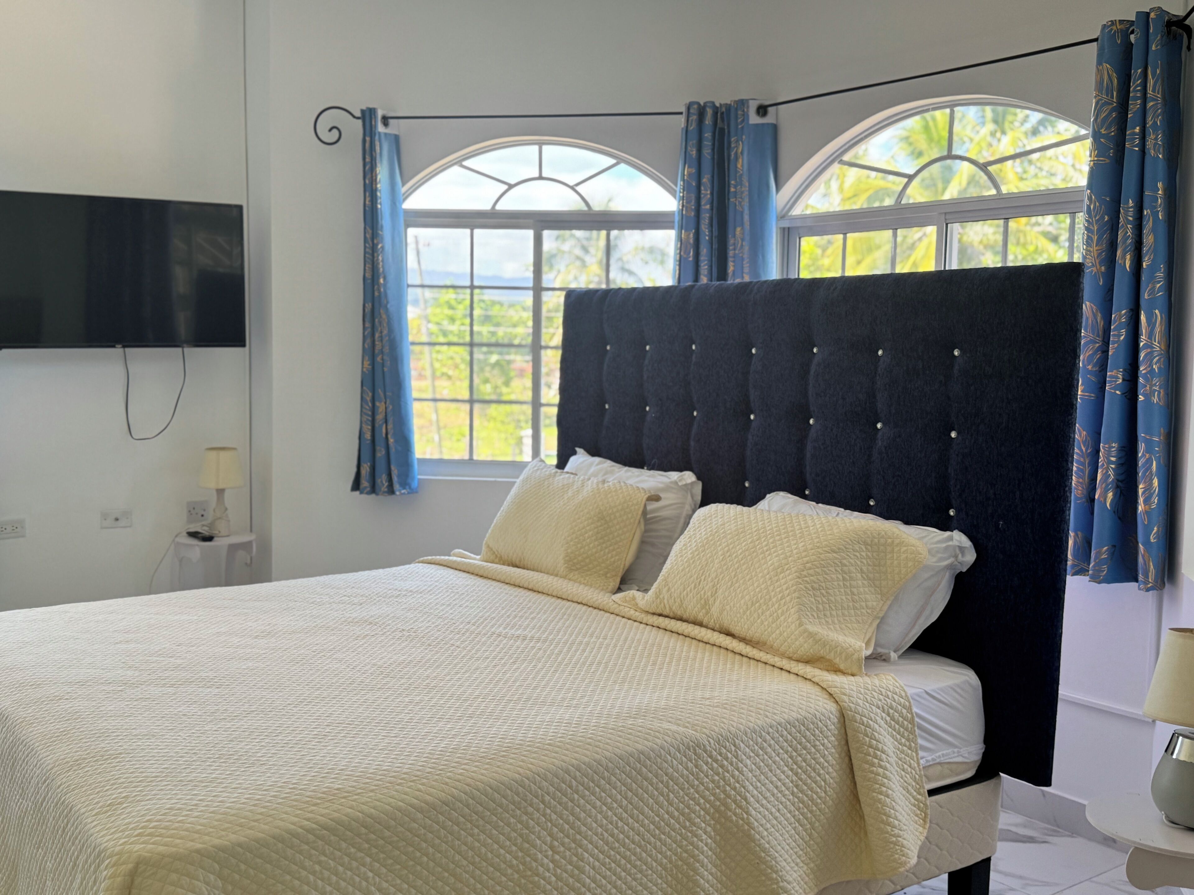 A bed with a quilted headboard, a bedside table, and a wall-mounted TV.