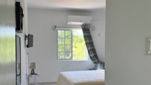 A bedroom with a bed, a window, a radiator, and a small table with a lamp.