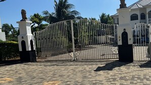 A gated entrance with a lion statue on each side, paved with interlocking bricks, and a clear sky above.