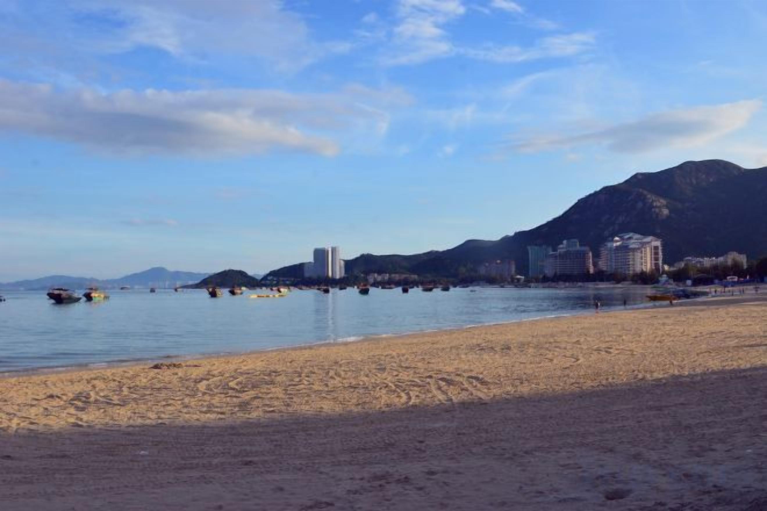 A beach with a clear sky, calm water, and buildings in the background.