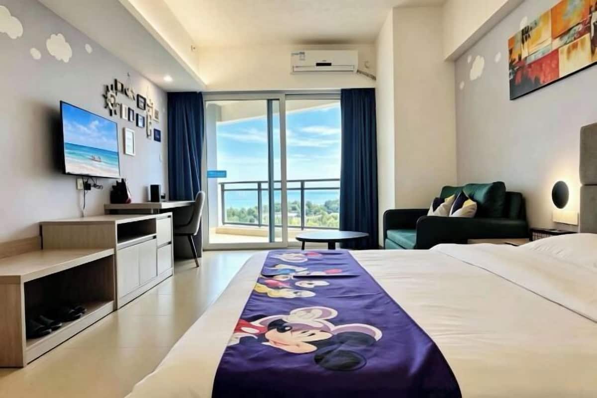 A hotel room with a bed, a desk, a chair, a TV, and a balcony with a view.