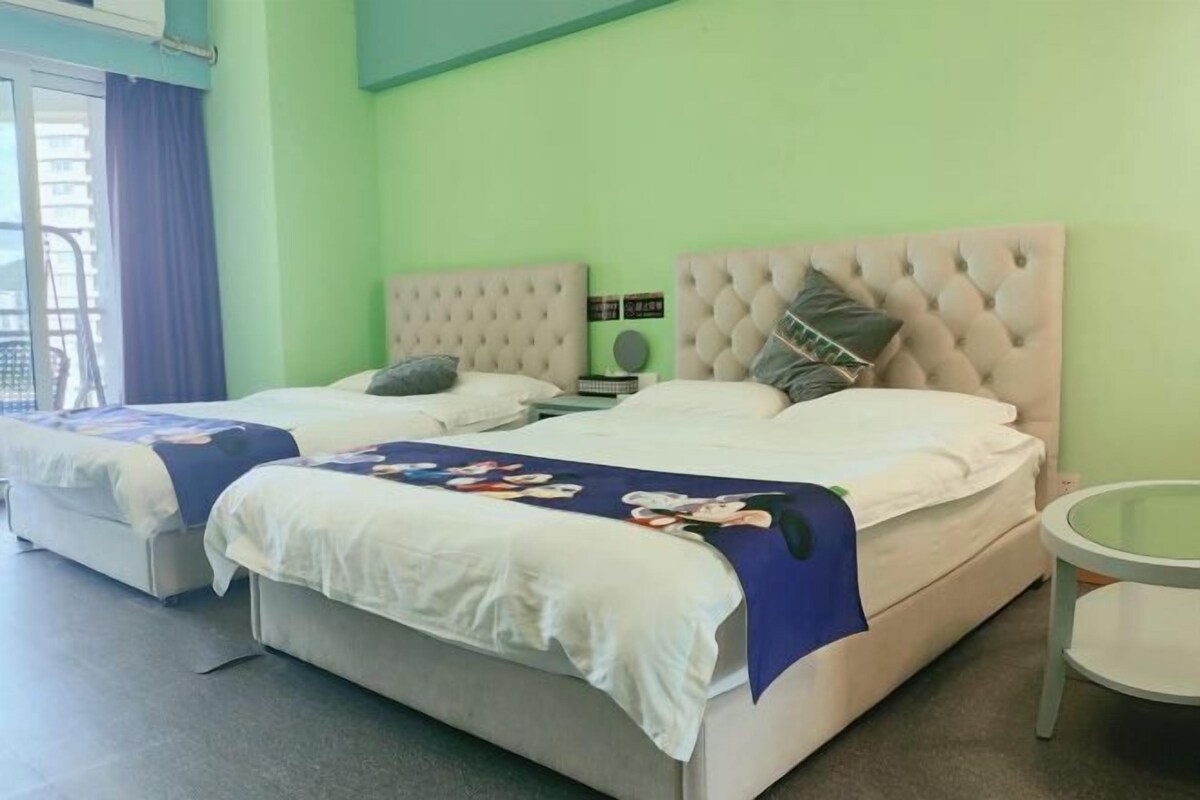 Une chambre d’hôtel avec deux lits, chacun doté d’une tête de lit capitonnée et de linge de lit blanc. On y trouve une petite table ronde et une fenêtre avec des rideaux.