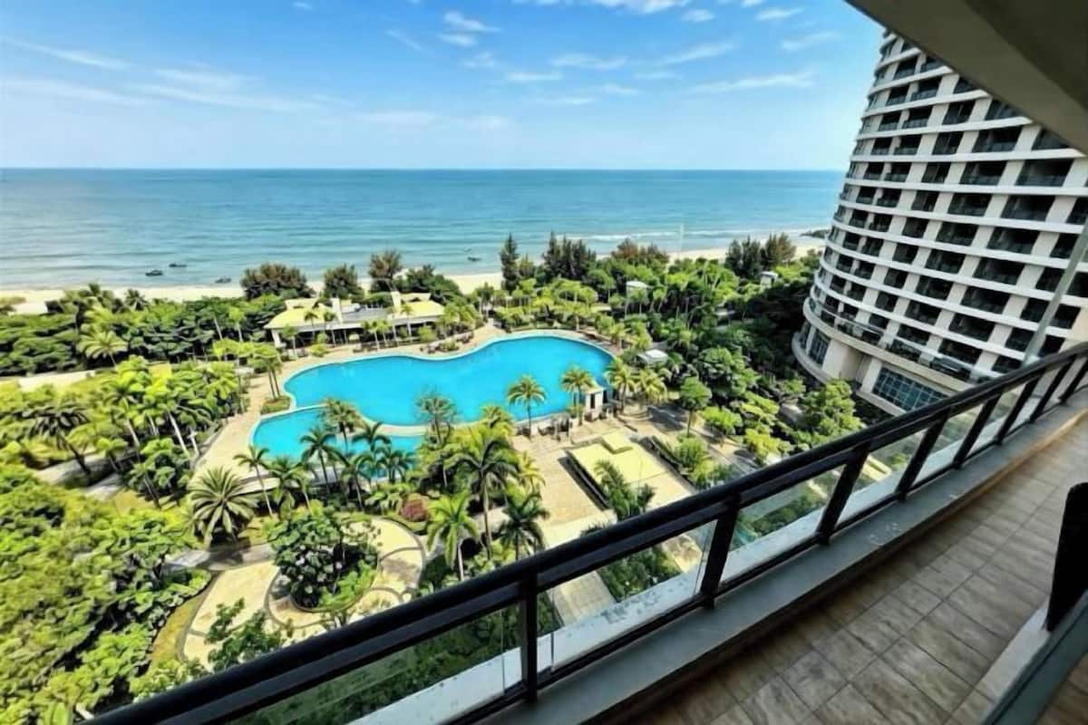 A hotel with a pool surrounded by palm trees and a view of the ocean.