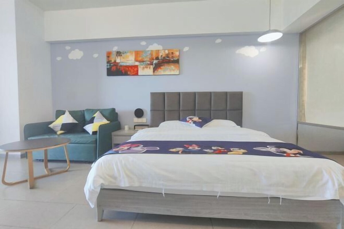 Une chambre à coucher avec un lit, un canapé, une petite table et un mur orné d’un tableau.