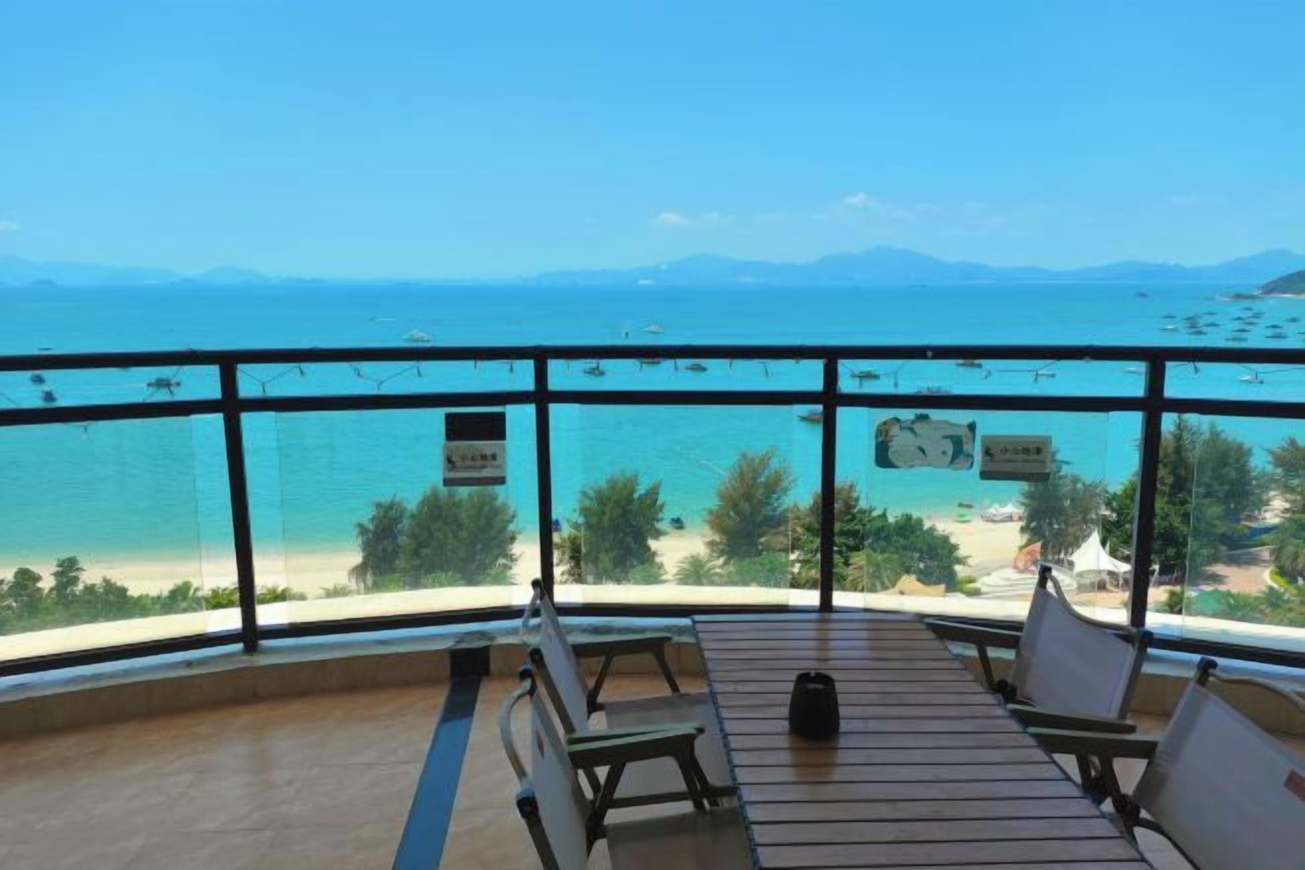 Un balcón con vista al mar y a las montañas, mobiliario de madera y un cartel con texto.
