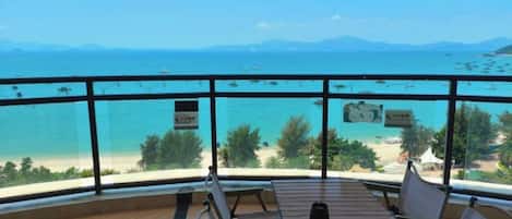 A balcony with a view of the sea and mountains, wooden furniture, and a sign with text.
