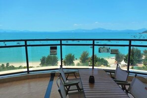 Un balcon avec vue sur la mer et les montagnes, des meubles en bois et une pancarte avec du texte.