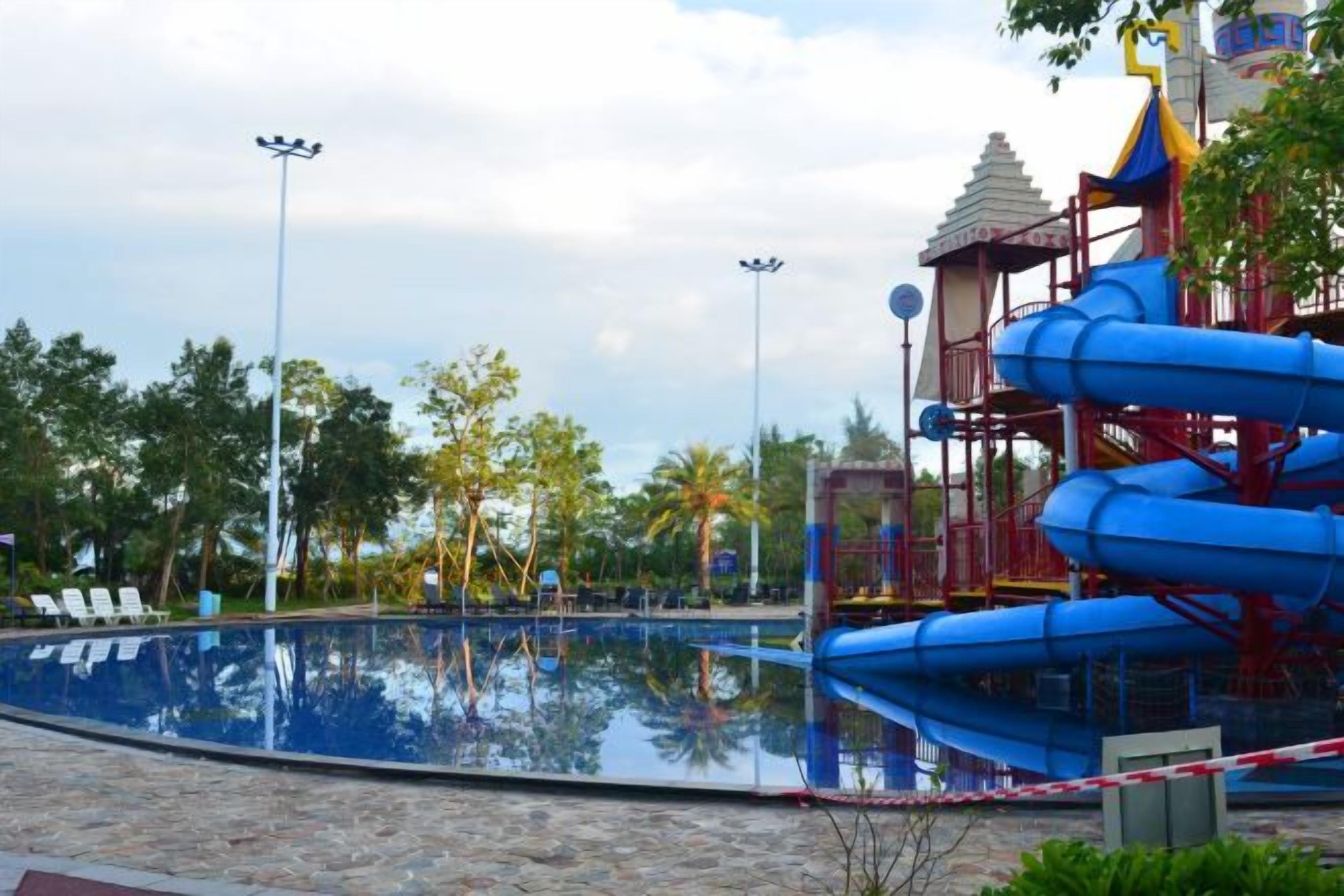 Une piscine avec un toboggan, entourée d’arbres et agrémentée d’un belvédère.