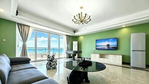 A modern living room with a sofa, a glass coffee table, a dog, a TV, and a view of the sea. - Huidong Xunliao Bay New Coast Scenic Hotel (Haigongyuan Leisure Beach) (Huidong)