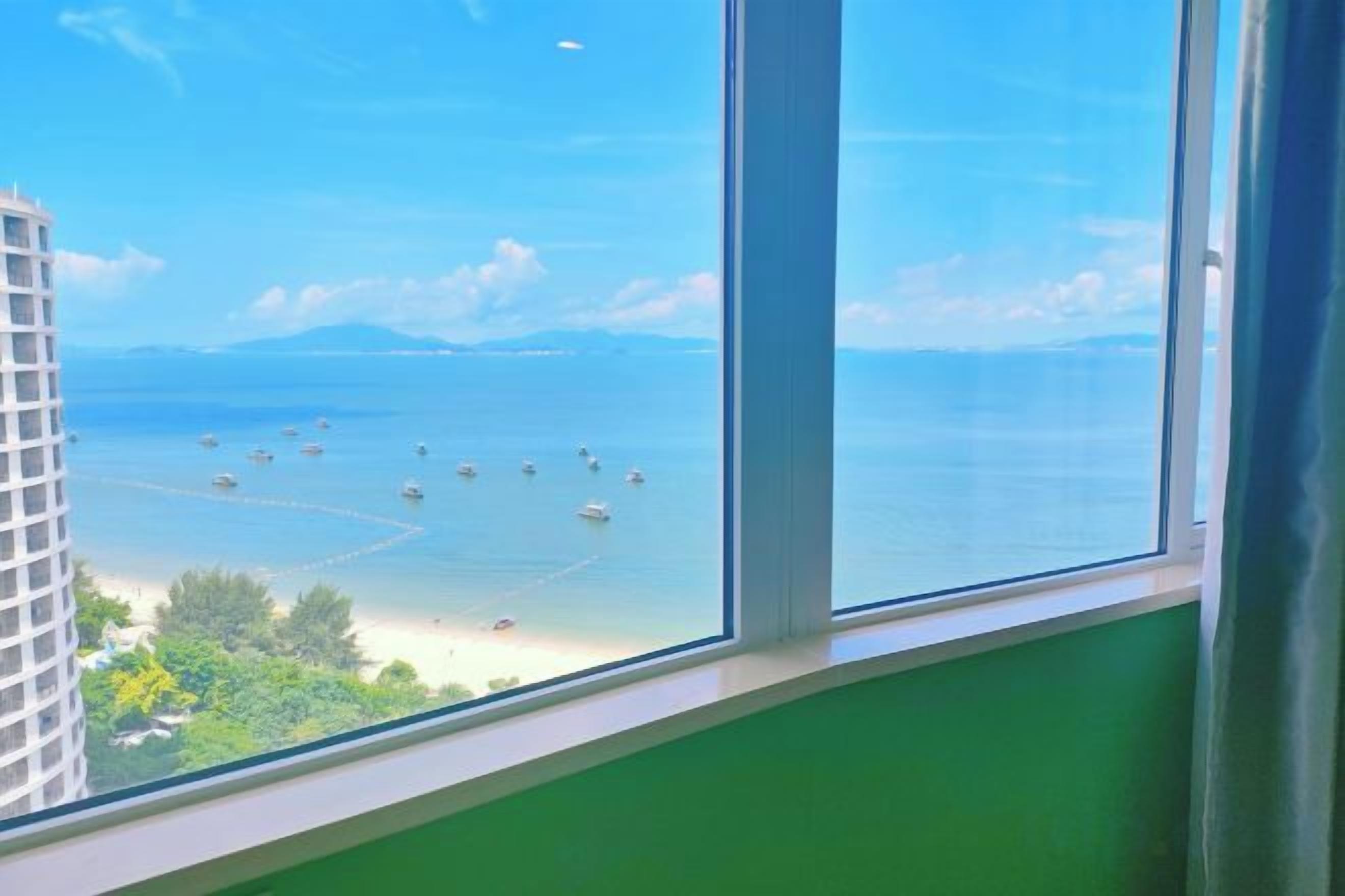 A view from a window overlooking a beach with boats, a clear sky, and a green building.