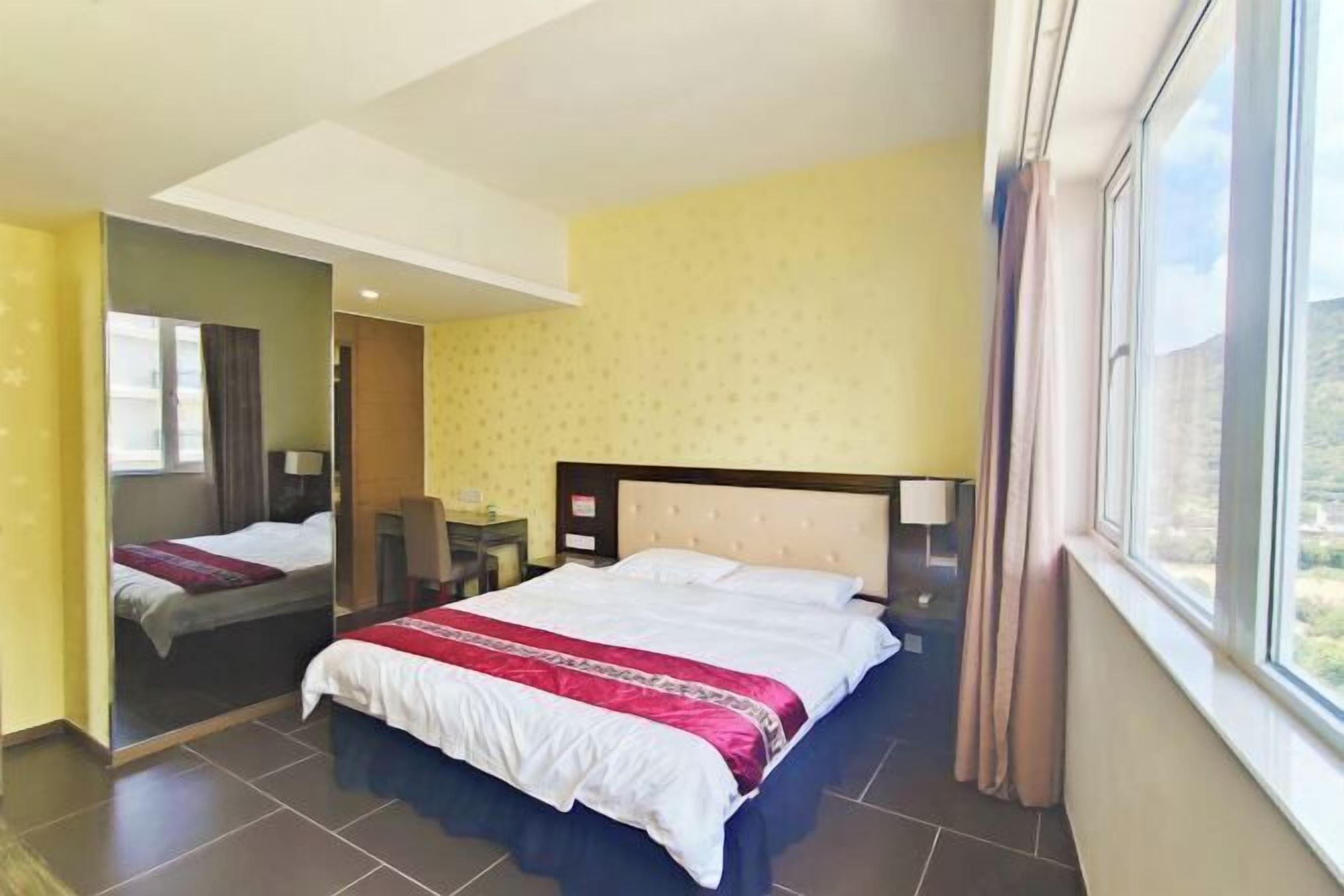 Quarto de hotel com uma cama grande, um espelho, uma escrivaninha e uma janela com cortinas.