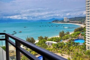 Une vue sur la côte depuis un balcon, avec une plage, des bateaux et une zone de villégiature comprenant une piscine et un toboggan aquatique.