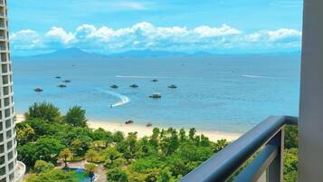 Vista de uma praia com barcos, céu claro e montanhas ao longe.