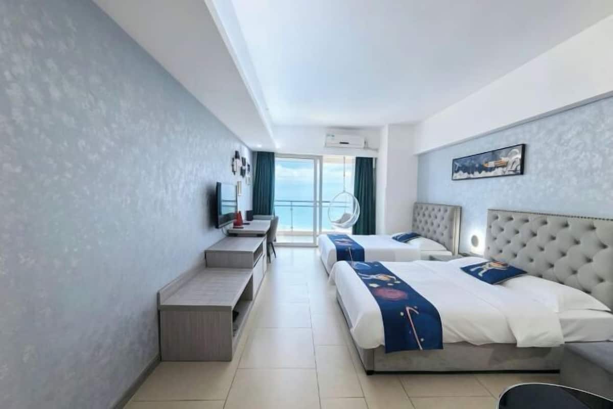 A hotel room with two beds, a desk, a chair, a TV, and a balcony with a view.