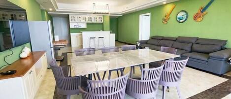 A dining area with a glass-top table and purple chairs, a grey sofa, and a chandelier.