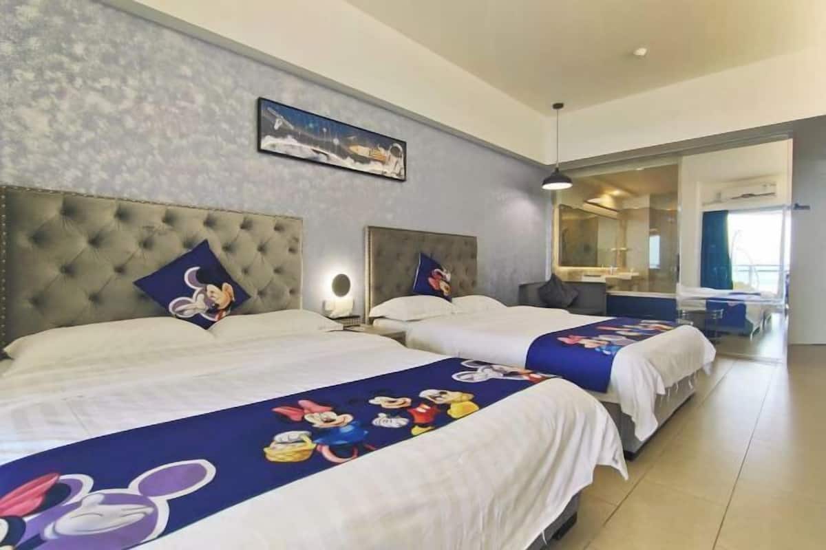 A hotel room with two beds, each with a Mickey Mouse themed bedspread. There is a large window with a view of the city, and a mirror on the wall.