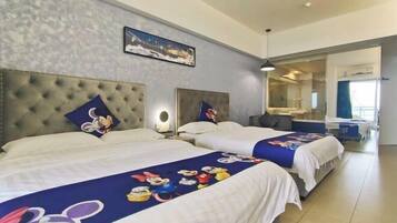 Quarto de hotel com duas camas, cada uma com colcha temática do Mickey Mouse. Há uma janela grande com vista para a cidade e um espelho na parede.